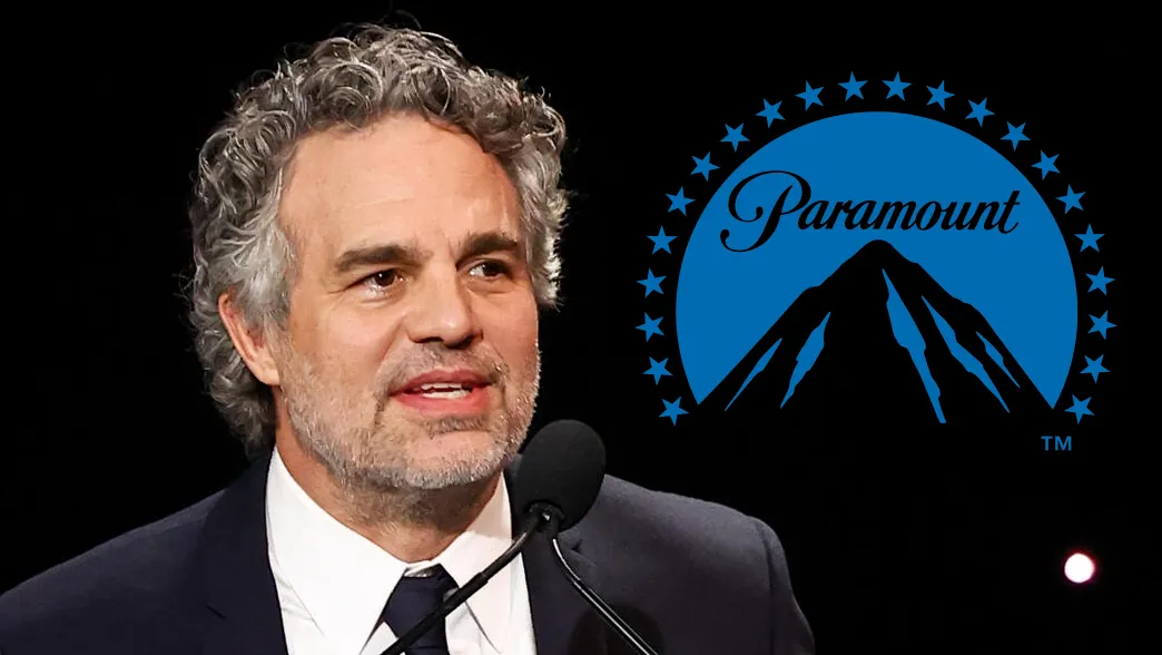 A gray-haired man in a suit speaks at a microphone beside a blue Paramount logo on a black background.