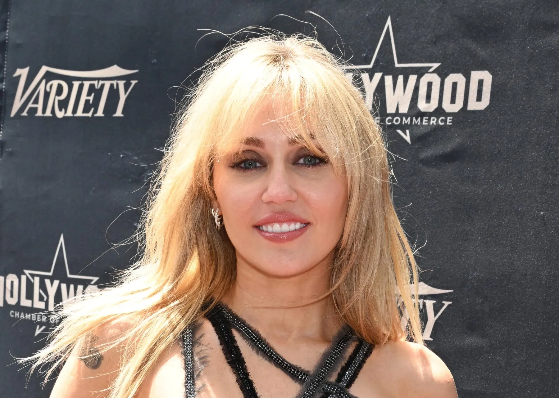 Blonde woman smiling in a black halter outfit before a backdrop with Variety and Hollywood Commerce logos.