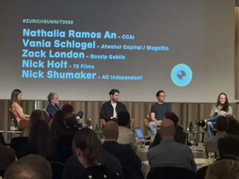 Five people sit onstage before an audience beneath a projection listing #ZURICHSUMMIT2026 and names.