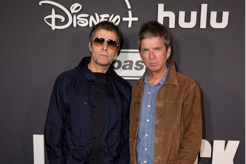 Two men stand before a backdrop with Disney+, Hulu, and Oasis logos.