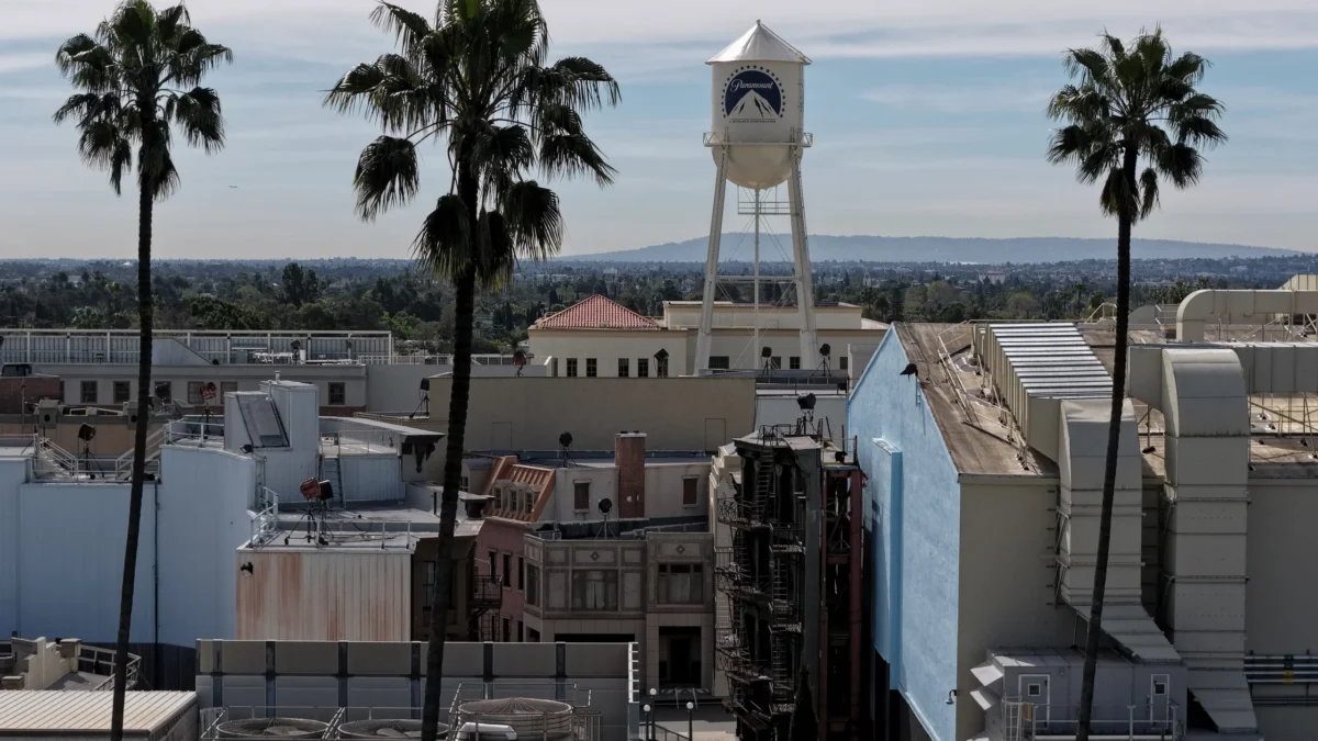 A Paramount-branded water tower rises above building rooftops and palm trees under a cloudy sky.