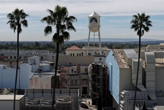 A Paramount-branded water tower rises above building rooftops and palm trees under a cloudy sky.