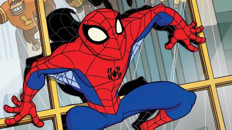 A masked superhero in a red and blue web-patterned suit crouches against a glass window.