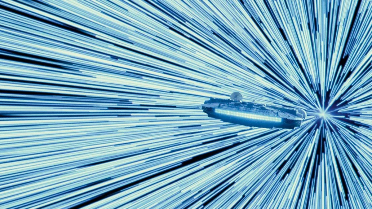 A spaceship flies through bright blue streaks of light converging in the distance.