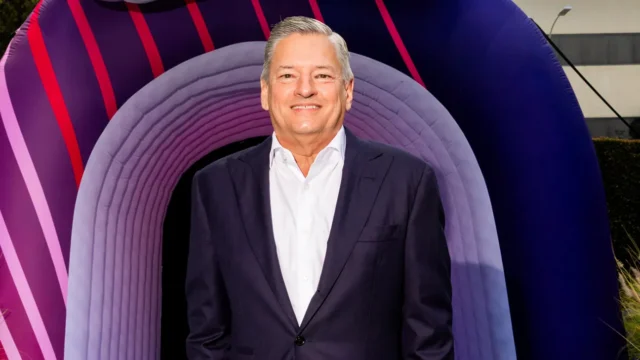 Smiling man in a dark suit stands before a large purple arch with red striped accents.