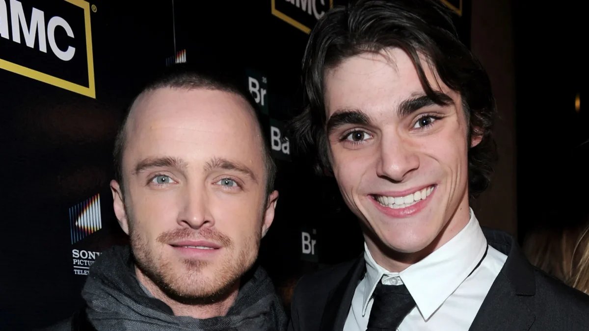 Two men pose closely at a black AMC-branded backdrop, one smiling broadly in a suit and tie.
