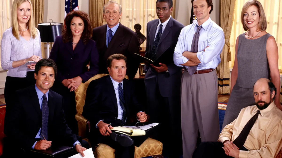 Nine formally dressed adults pose together in a stately room with flags, curtains, papers, and notebooks.