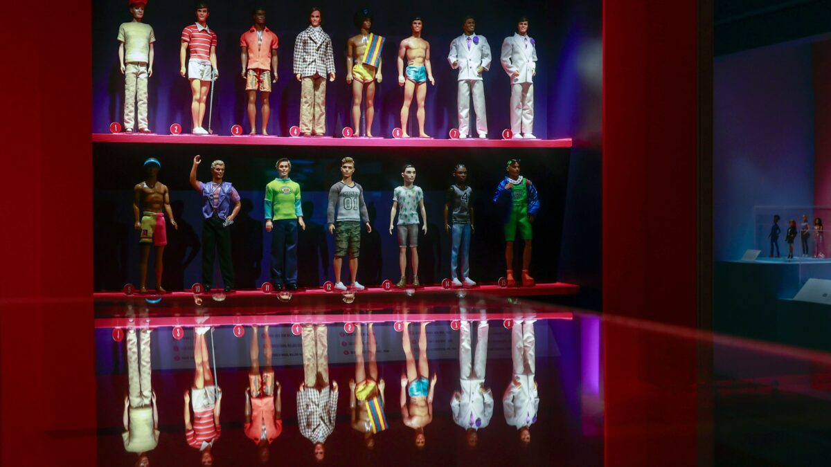 Dolls in varied outfits stand on numbered shelves inside a red-lit display case.