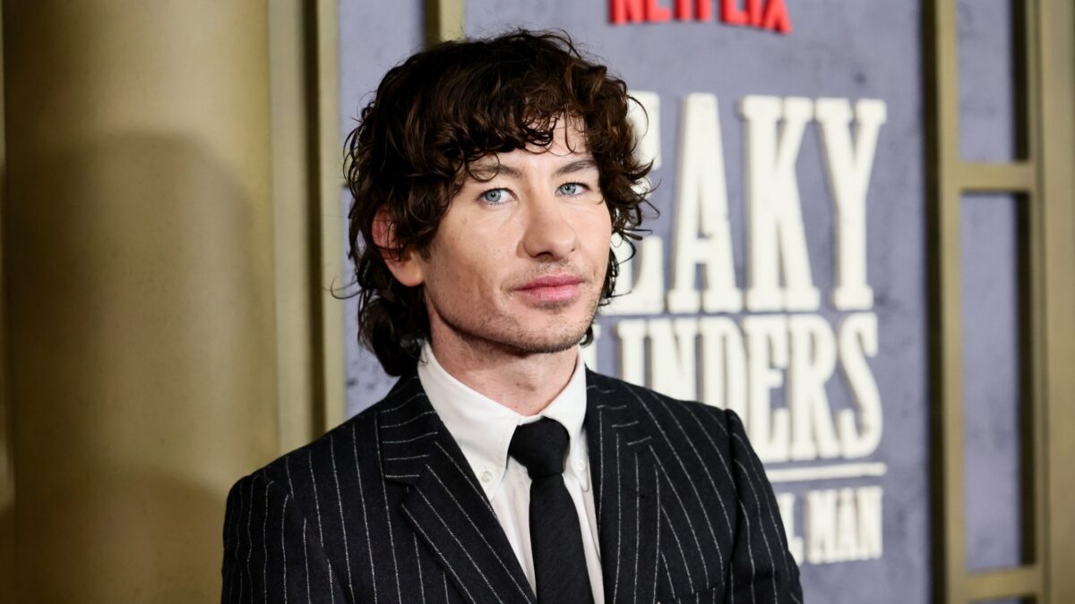 Curly-haired man in a pinstripe suit poses in front of a Netflix backdrop.