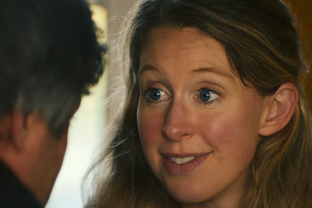 A woman with blue eyes smiles while facing a person seen from behind in soft indoor light.