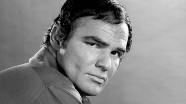 Black-and-white close-up of a dark-haired man looking over his shoulder against a plain background.