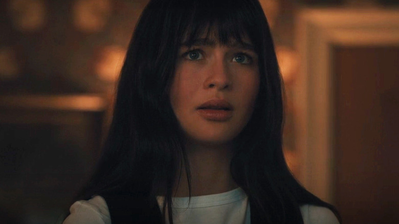 Young woman with long dark hair and bangs looks worried in a dimly lit room.