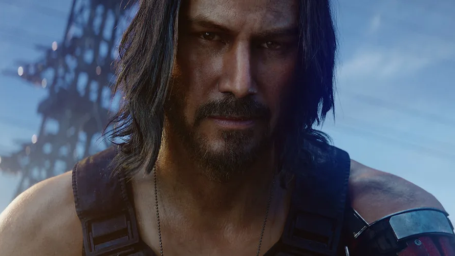 A long-haired bearded man in tactical gear stares intensely against a blurred blue industrial background.