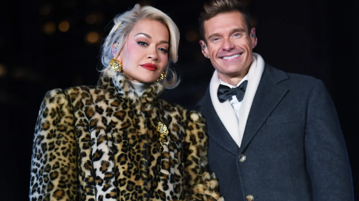 Two people pose against a dark background, one in a leopard-print coat and one in a gray coat.