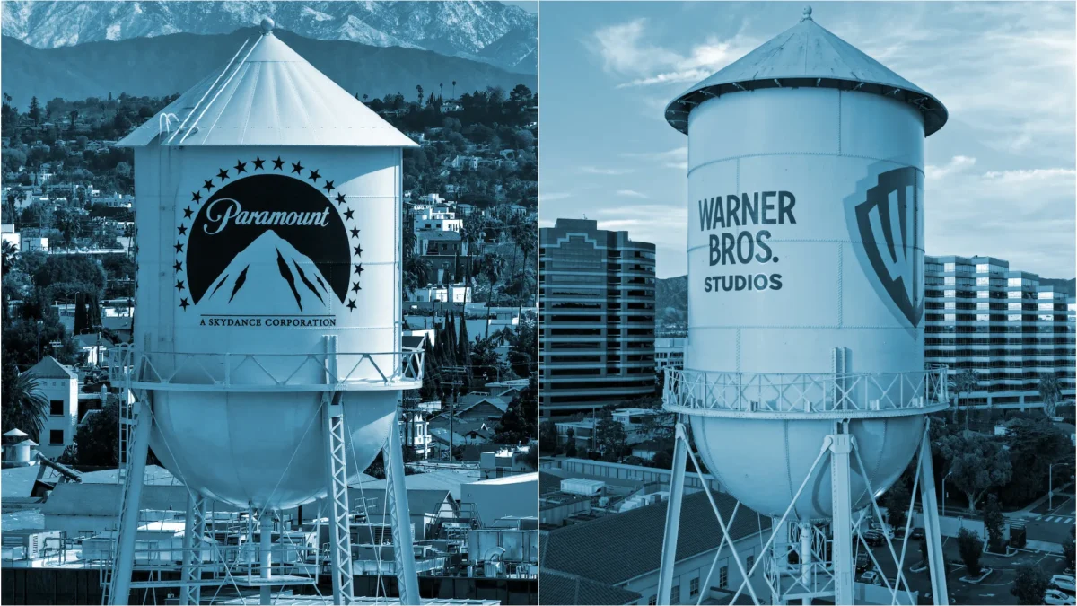 Two large water towers display Paramount and Warner Bros. Studios logos amid city buildings and mountains.
