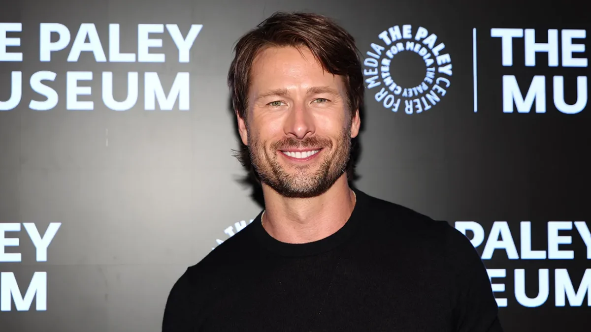 A smiling man in a black shirt stands before a dark backdrop with Paley Museum logos.