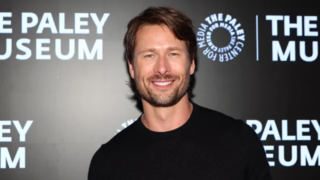A smiling man in a black shirt stands before a dark backdrop with Paley Museum logos.