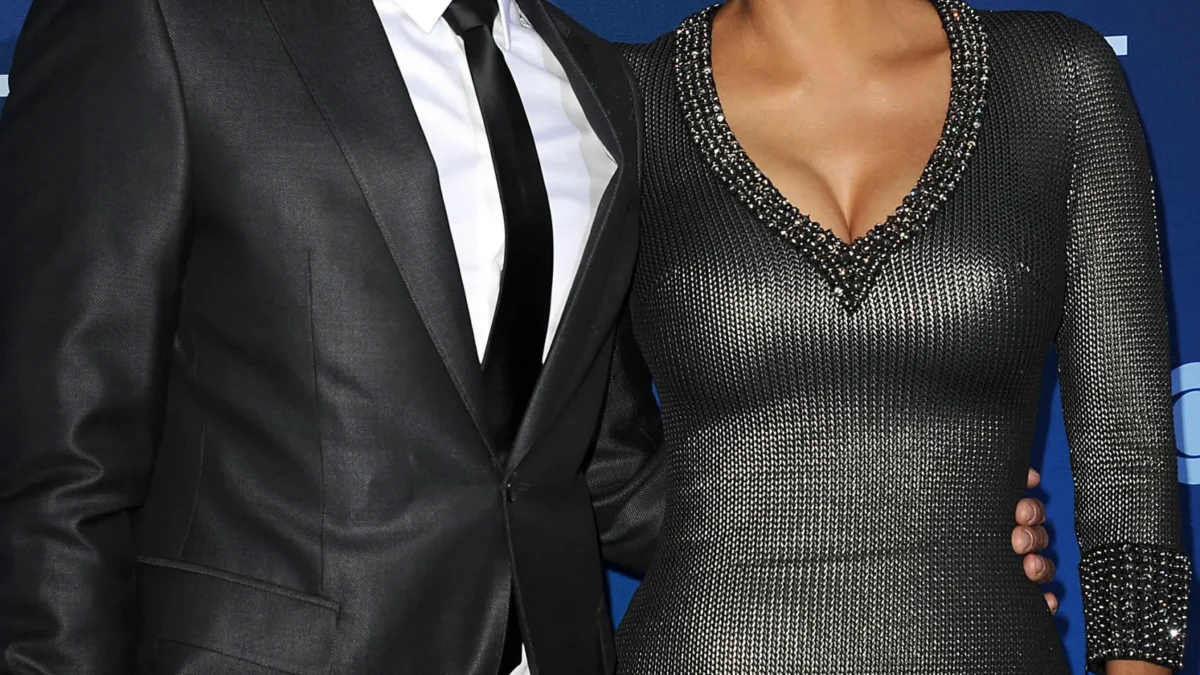 Two formally dressed people pose together in front of a blue backdrop with white logos.
