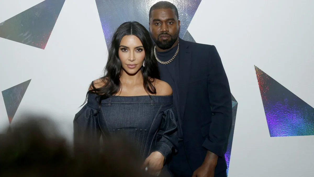 Two people pose in front of a white wall with reflective geometric shapes.