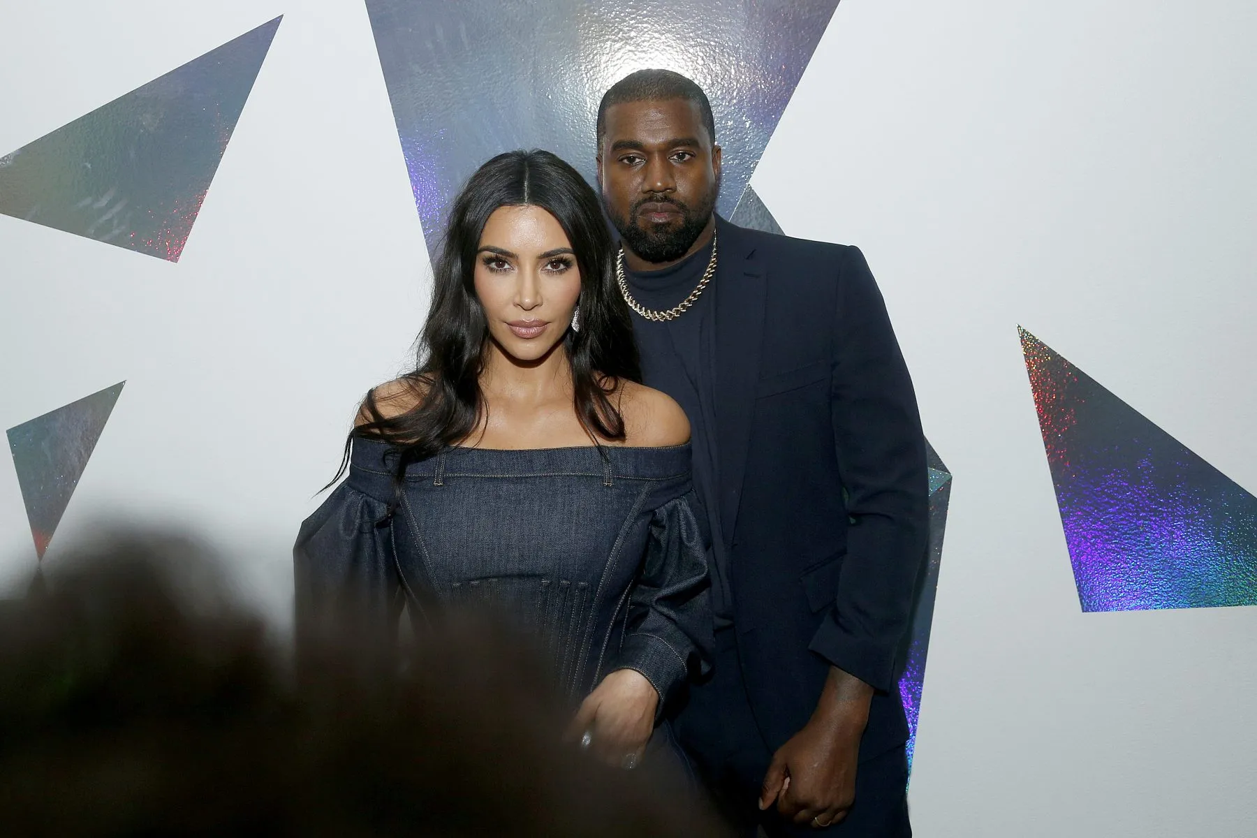 Two people pose in front of a white wall with reflective geometric shapes.