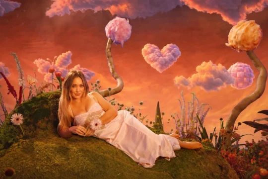 A woman in a white dress reclines in a whimsical garden under orange skies and heart-shaped clouds.