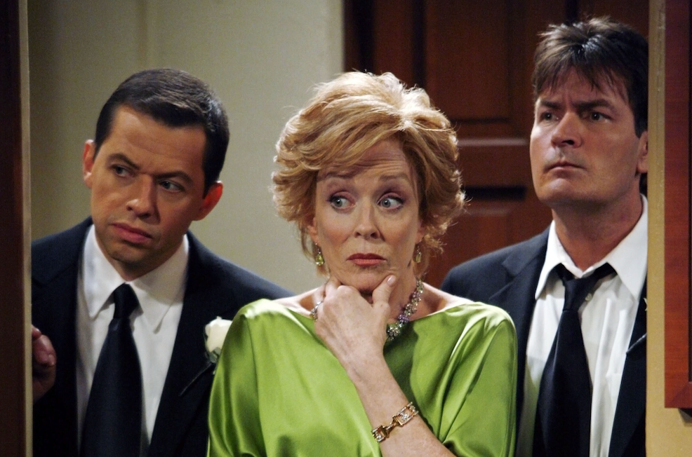 Three formally dressed people stand in a doorway, with a woman in green looking sideways between two men.