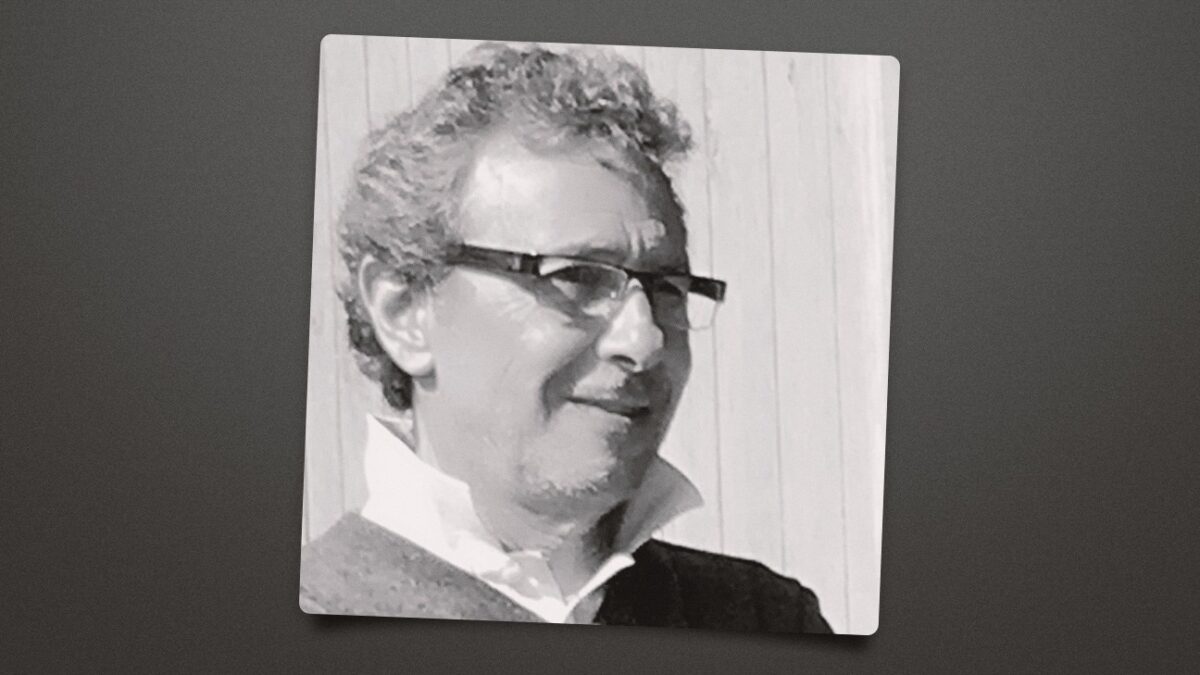 Black-and-white portrait of a man wearing sunglasses and a collared shirt, shown on a tilted print.