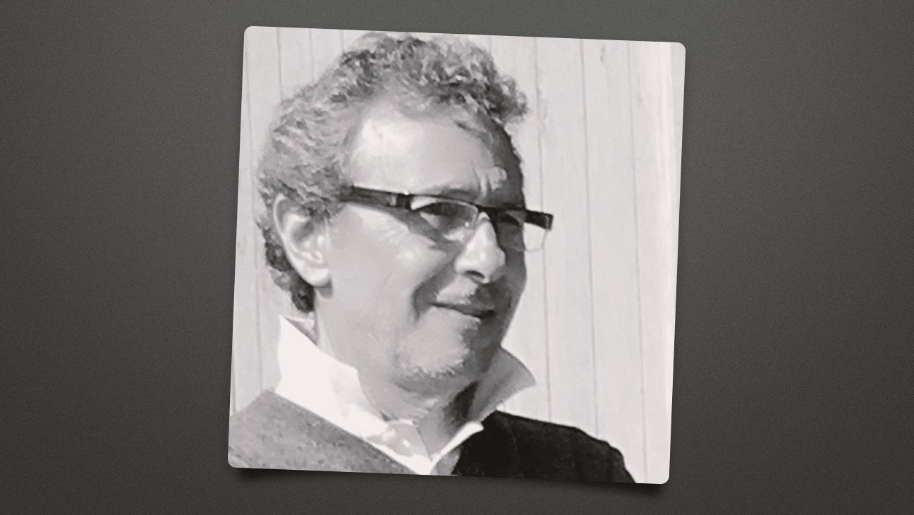 Black-and-white portrait of a man wearing sunglasses and a collared shirt, shown on a tilted print.