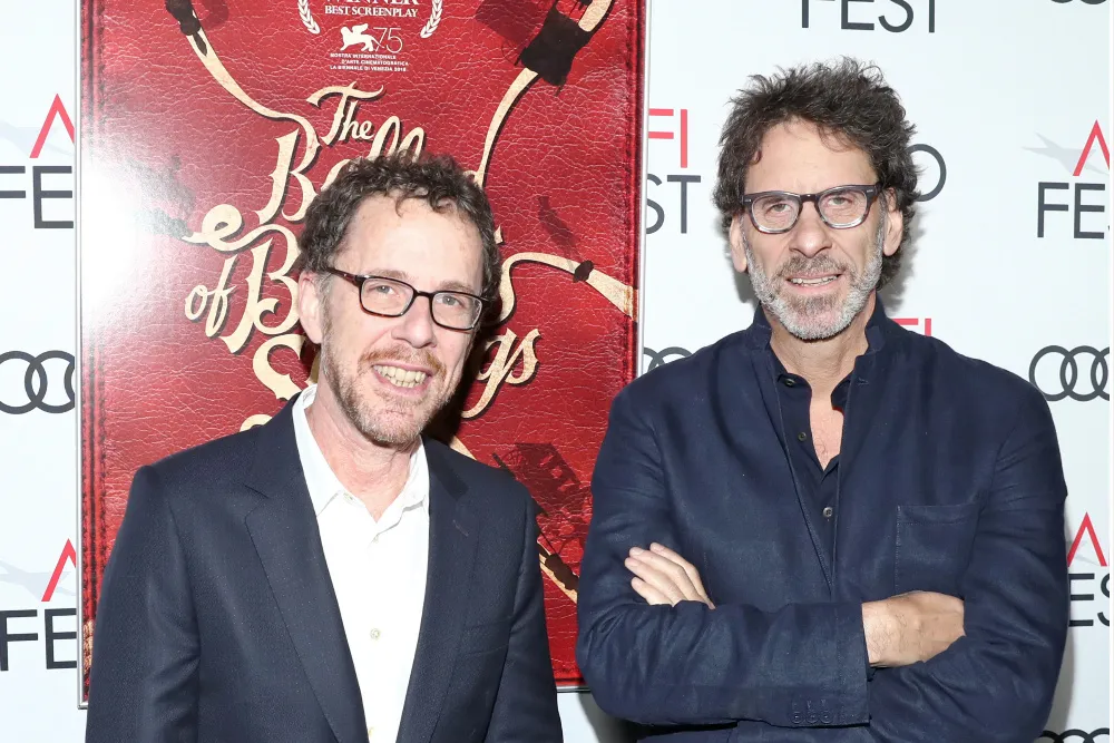 Two men in dark jackets and glasses pose before a red movie poster and festival-branded backdrop.
