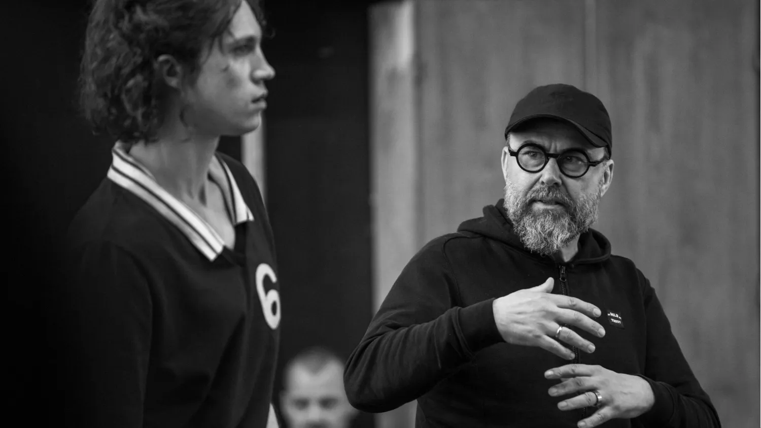 A bearded man in glasses and cap gestures beside a young man wearing a numbered jersey.