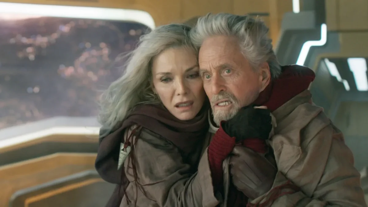 A gray-haired man and blonde woman huddle together in a futuristic room, looking concerned.