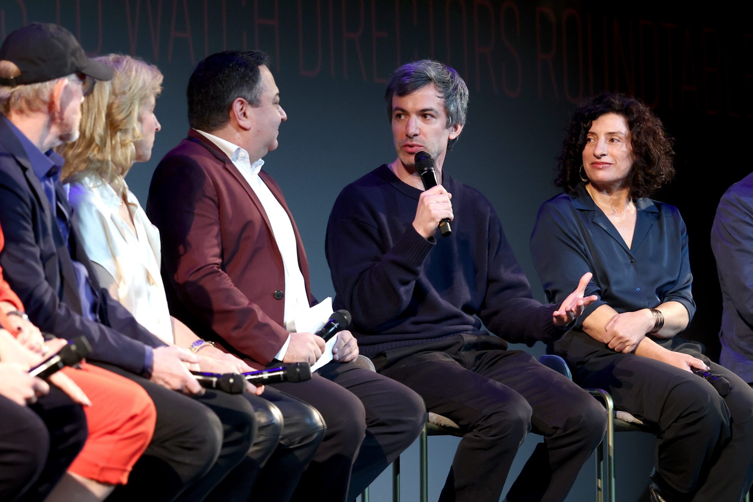 A seated panel of people, with one man speaking into a handheld microphone while others listen.