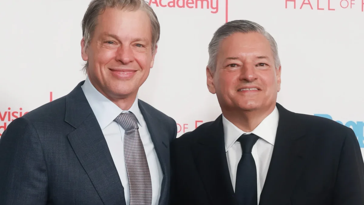 Two men in suits smile in front of a Television Academy backdrop.