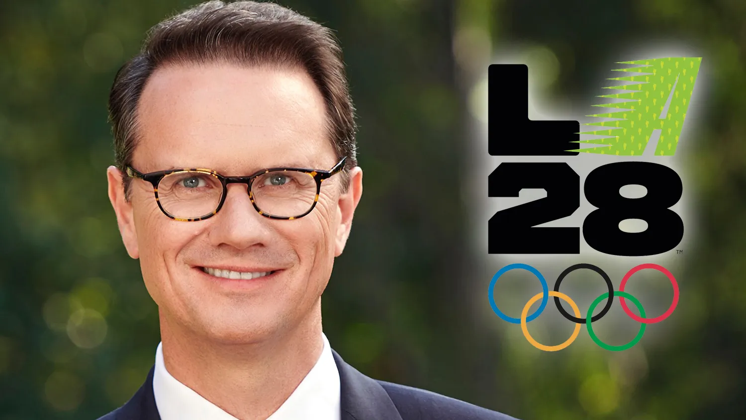 A smiling man in glasses and a suit appears beside the LA28 logo and Olympic rings.