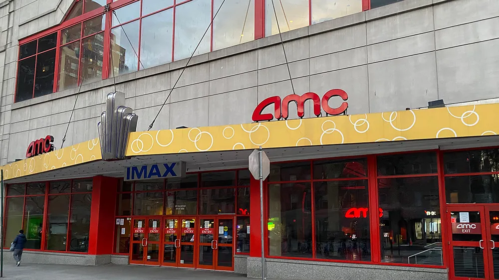 AMC building facade with red-framed windows, a yellow marquee, IMAX sign, and glass entrance doors.
