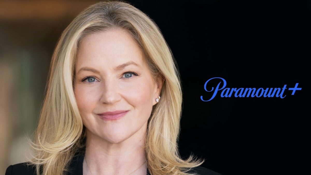 A blonde woman in a black blazer smiles beside a blue Paramount+ logo on a dark background.