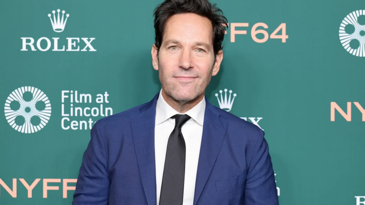 A man in a blue suit and black tie stands before a green backdrop with Rolex and NYFF logos.