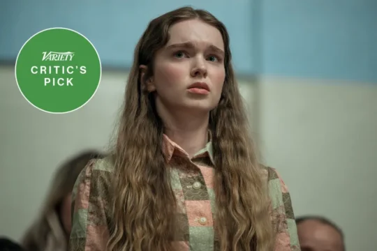 A young woman with long wavy hair looks worried beside a green “Critic’s Pick” badge.