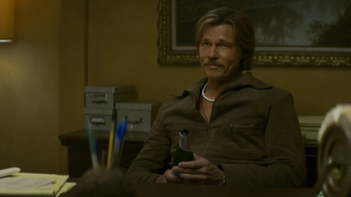 "A man with a mustache sits at a desk in a warmly lit office, holding a green bottle. The room has a lamp, filing boxes, and papers, with a painting and organized supplies in the background."
