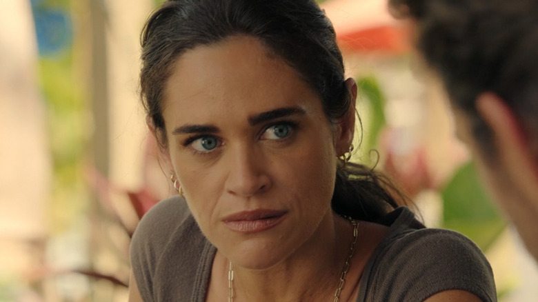 A woman with dark hair looks intently at a blurred person in a warm, softly lit setting.