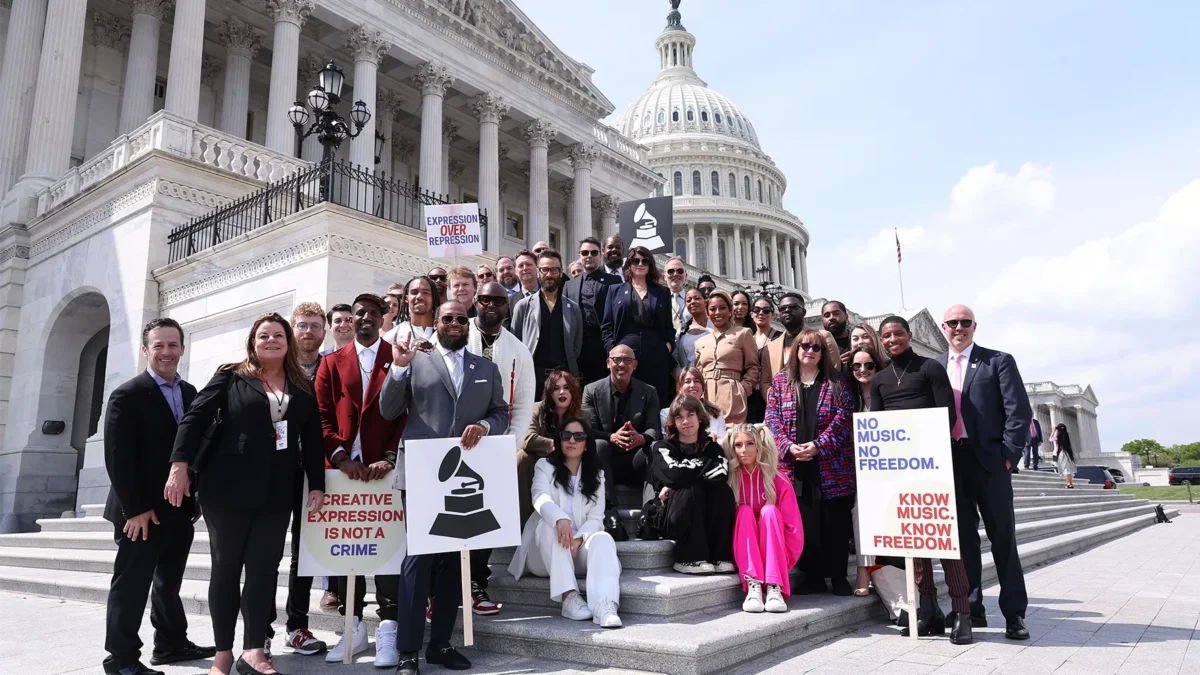 A large group poses on steps outside a domed neoclassical building, holding signs about music and expression.