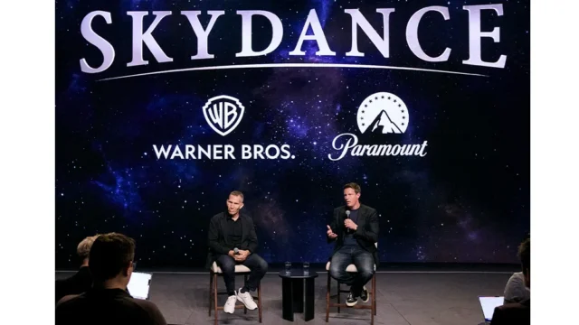 Two men sit with microphones onstage before a starry screen displaying Skydance, Warner Bros., and Paramount logos.