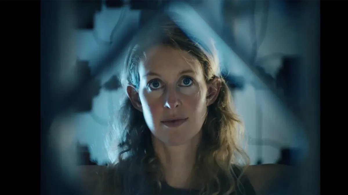 A woman with curly hair stares forward through blue-lit translucent geometric shapes.