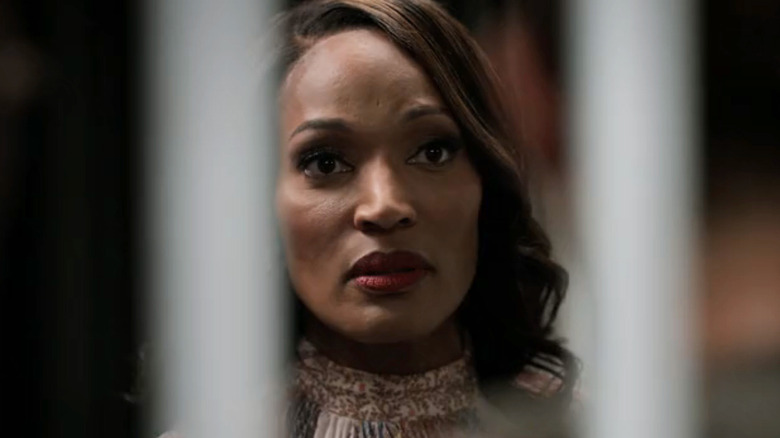 A woman with a serious expression looks ahead from behind blurred vertical bars.