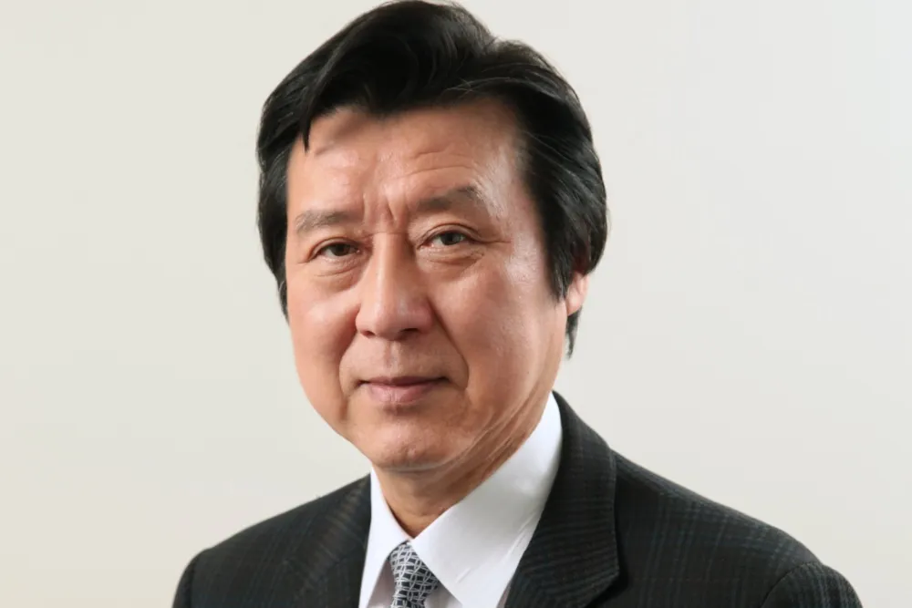 A man in a dark suit and patterned tie poses against a plain light background.