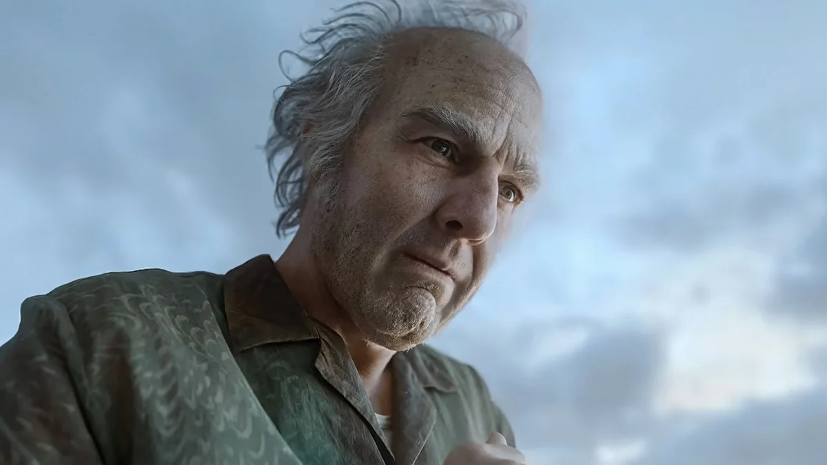 Close-up of an older man with windblown gray hair and a patterned shirt against a cloudy sky.