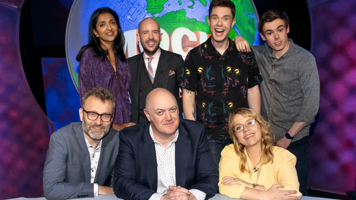 Seven people pose in a studio before a large colorful globe backdrop.