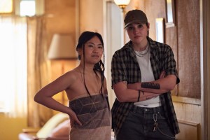 Two people stand in a warmly lit room, one with a hand on their hip and one with arms crossed.