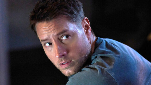 A man in a blue shirt looks over his shoulder with a tense expression in dim lighting.