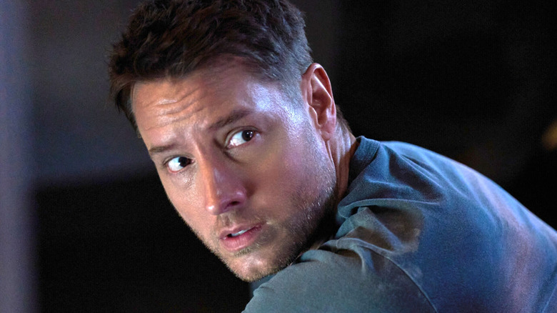 A man in a blue shirt looks over his shoulder with a tense expression in dim lighting.